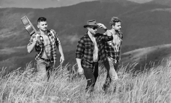 Adventurers squad. Tourists hiking concept. Group of young people in checkered shirts walking together on top of mountain. Men with guitar hiking on sunny day. Hiking with friends. Long route