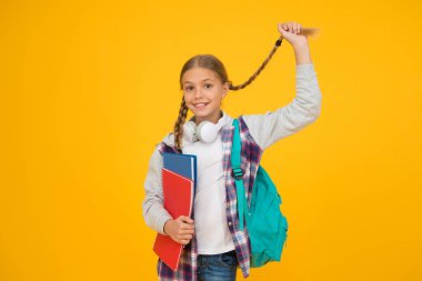 Uzun ve örgülü. Sevimli küçük okul çocuğu sarı arka planda uzun saç örgüsü tutuyor. Sevimli küçük kız uzun saç stili giyiyor. Okul için uzun saç stili