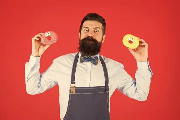 Restauration de produits de boulangerie pour vous. Un barbu tenant des beignets dans une boulangerie. Boulanger professionnel avec des aliments de boulangerie vitrée sur fond rouge. Les beignets parfaits de notre boulangerie — Photo