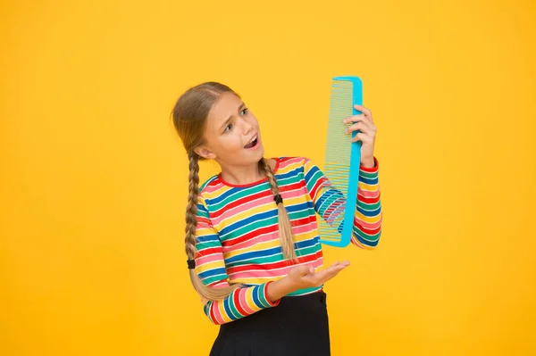 Professional equipment. Combing hair. Cheerful happy smiling little kid with giant comb. Comb for tangled hair. Hairdresser supplies. Large comb. Girl long hair hold enormous comb. Hairdresser salon