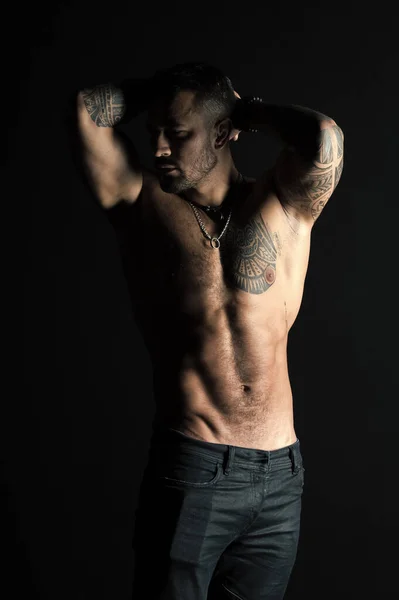 Homem tatuado mostra torso muscular sexy. Esportista com seis maços e abdominais. Fisiculturista com bíceps e tríceps. Modelo de moda com tatuagem em jeans. Cuidado com o corpo com fitness e esporte — Fotografia de Stock