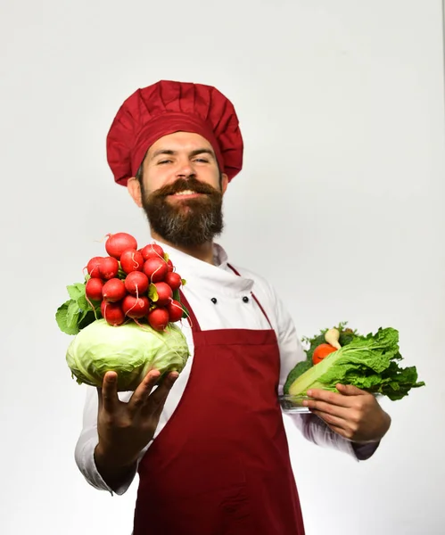 Cocinar con una sonrisa orgullosa en uniforme sostiene la col y el rábano —  Fotos de Stock