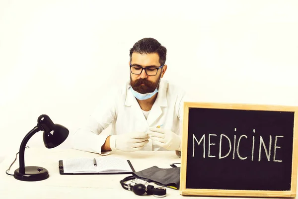 Médico caucasiano barbudo sentado à mesa com placa Medicina inscrição — Fotografia de Stock