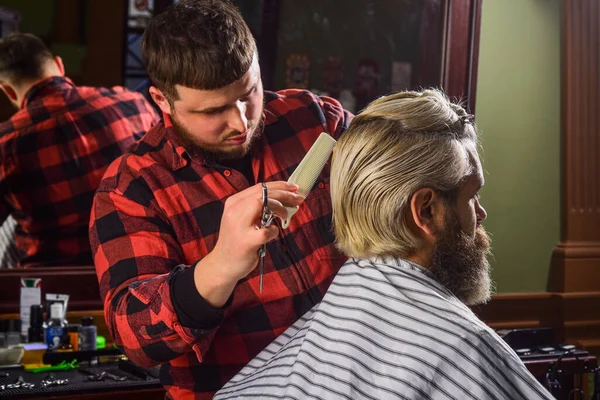 Barbiere parrucchiere. L'hipster si taglia i capelli. L'oggetto affilato vicino a faccia e contorcersi distrae la persona che lo tiene. Dona i capelli. Concetto di donazione e carità. Un tizio con i capelli biondi tinti. Capelli tagliati — Foto Stock