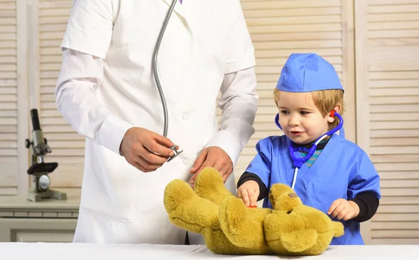 Pediatra y pequeño asistente examinan osito de peluche —  Fotos de Stock