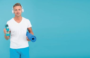 Spor içeceğini akıllıca seç. Sporcu adam spor şişesini ve paspası tutuyor. Yakışıklı, mavi bir geçmişi var. Sporcular için hidrasyon. Spor ve diyet. Sağlık ve eğlence. Sporda akışkanlar, boşluğu kopyala