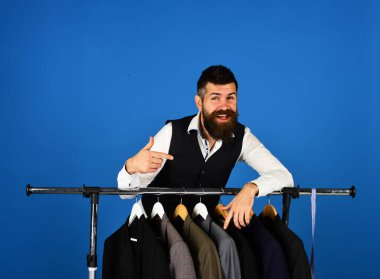 Elbise rafında sakallı bir adam. Mutlu yüzlü terzi.