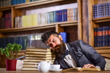 Çok çalışan bir adam açık bir kitabın üzerinde uyur ve masada daha fazlası vardır.