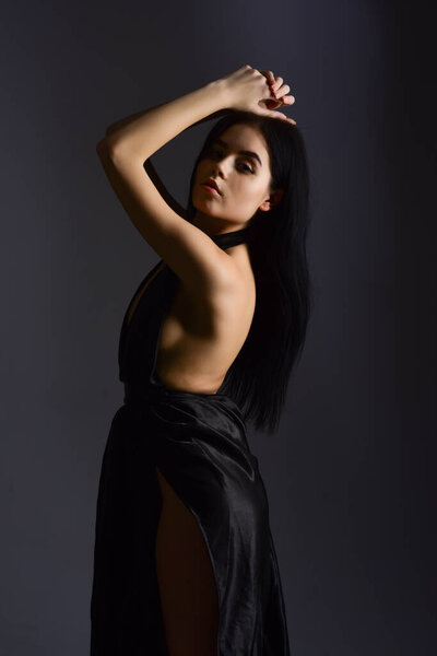 Attractive girl wears expensive fashionable evening dress with nude shoulders. Woman in elegant black dress with naked back, dark background. Desire concept. Lady, confident sexy girl in dress.