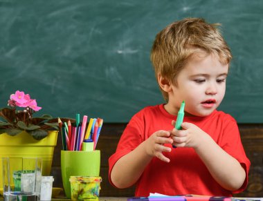Sanat sınıfındaki sarışın çocuk. Küçük sanatçı çizimi için doğru rengi arıyor..