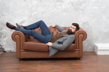 İnsanın kendine güveni böyle olur işte. Sakallı adam kanepede rahatla. İş hayatında kaba bir adam. Moda modası. Moda tarzı. Sakallı ve bıyıklı traşsız bir adam. Berber dükkanı. Kuaför salonu.