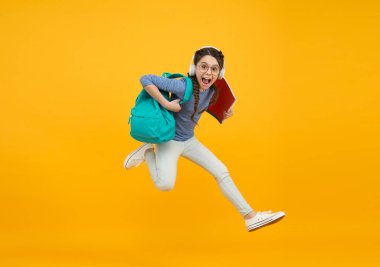 Zıpla bakalım. Enerjik kız okula sarı arka planda koşuyor. Mutlu çocuk okula geri döndü. Çocukluk aktivitesi. Eğitim ve kalkınma. Aktif yaşam tarzı. Geleceğine koş.