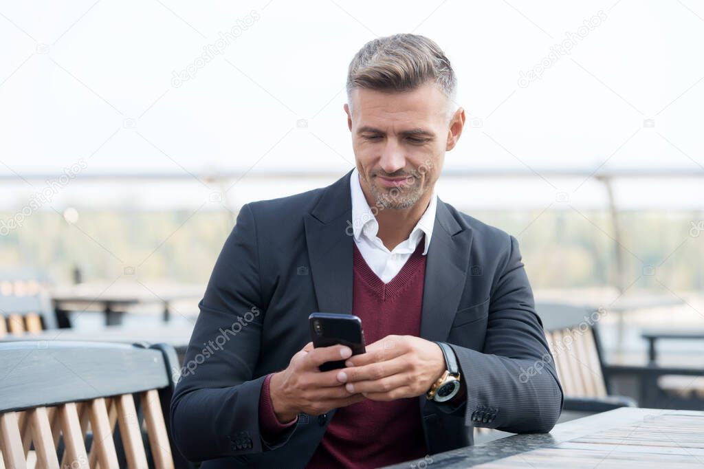 SMS survey. Happy businessman text sms in outdoor cafe. Texting SMS via smartphone. Business meeting. Mobile communication. SMS messaging. Short message service. New technology. Modern life. 3G. 4G