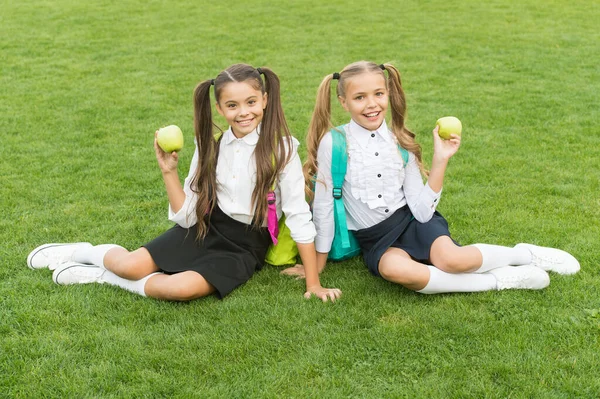 Cieszymy się przerwą na przekąski. Szczęśliwe dziewczyny jedzą jabłka na zielonej trawie. Biorę witaminę. Szkolna przekąska. Zdrowe jedzenie i przekąski. Wegetariańskie jedzenie. Dieta i dieta. Śniadanie albo lunch. Jedz i ucz się — Zdjęcie stockowe