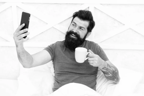 Nehir kahvesi. Mutlu hipster kahve içer, yatakta video görüşmesi yapar. Sakallı adam kahveden ve konuşmaktan hoşlanır. Sabah kahvesi rutini. Sosyal medya. Yeni teknoloji. Modern hayat. Gerçek zamanlı yayın — Stok fotoğraf