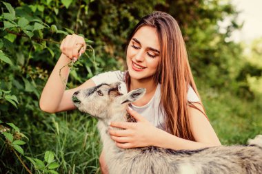 Kadın ve küçük keçi yeşili çimenler. Eko çiftliği. Sevgi ve ilgi. Hayvan hukuku. Çiftlik ve tarım kavramı. Köy hayvanları. Kız sevimli keçiyi oynuyor. Beslenen hayvan. Hayvanları korumak. Veteriner mesleği