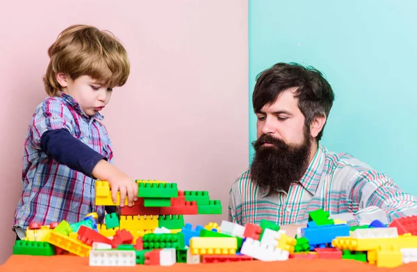 Child care and upbringing. Father son game. Father son create constructions. Father and boy play together. Dad and kid build plastic blocks. Father leader showing boy how grow into successful man