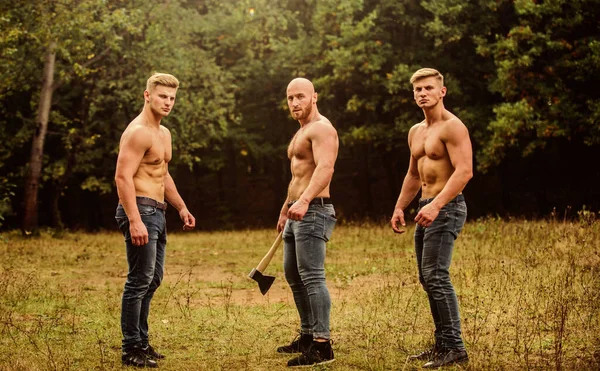 3人のセクシーな男残忍な男は裸の胴でポーズ。セクシーな体をしたハンサムな男スポーツやレジャー。メソモルフ斧を持つ筋肉質の男3人運動選手は斧を使うジーンズのボディビルダー — ストック写真