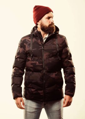 Sakallı adam beyaz arka planda izole edilmiş sıcak kamuflaj desenli ceket giyiyor. Hipster kış modası. Şapka takan ve siyah kışlık ceket giyen adam. Rahat bir kış kıyafeti. Kış stili erkek giyim