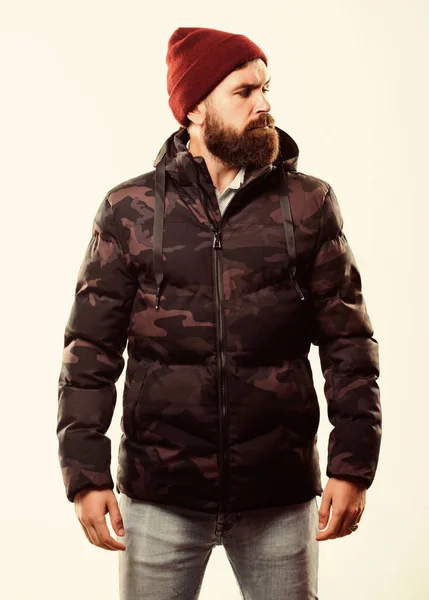 Man γενειοφόρος σταθεί ζεστό καμουφλάζ μοτίβο σακάκι paka απομονώνονται σε λευκό φόντο. Χειμωνιάτικη μόδα. Ο τύπος φοράει καπέλο και μαύρο χειμωνιάτικο μπουφάν. Άνετα χειμωνιάτικα. Χειμώνας κομψό ανδρικό ένδυμα — Φωτογραφία Αρχείου