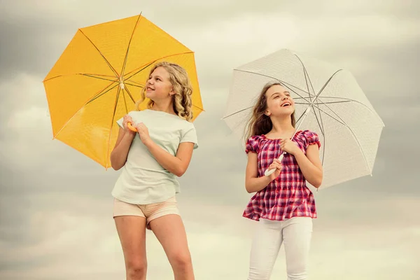 Bambini spensierati all'aperto. Libertà e freschezza. Previsioni meteo. Pronti per qualsiasi tempo. Vento o piovoso siamo preparati. Il tempo cambia. Ragazze amiche con ombrelli cielo nuvoloso sfondo — Foto Stock