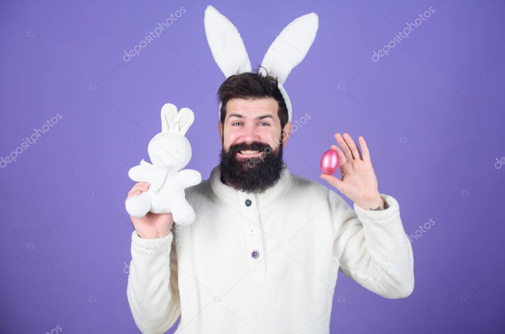 Easter bunny hunt begins. Happy man with rabbit ears holding bunny toy and egg. Bearded man in rabbit costume with easter egg and hare toy. Spring, new life and fertility. Spring holiday celebration