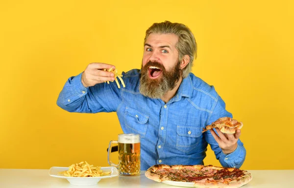 Neşeli sakallı hippi adam pizza yiyor. Barda akşam yemeği. Aç adam pizza yiyecek ve bira içecek. Pizzacı. Pizza partisi konsepti. Mutluluğu ağıza vermek. Bira ve yemek. — Stok fotoğraf