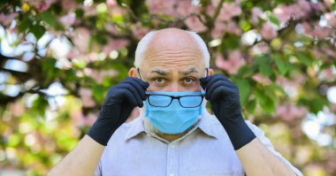 Virüs enfeksiyonundan koru. Enfeksiyonun yayılma riskini sınırla. Enfeksiyon havada. Son sınıflar covid-19 hakkındaki yanlış bilgilere inanıyorlar. Dışarıda maske ve eldiven takan kıdemli bir adam var.