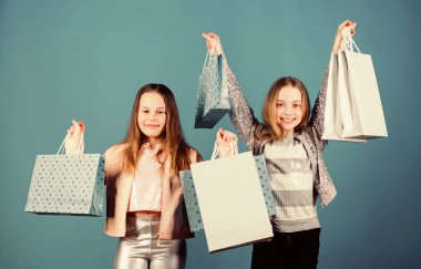 Mutlu çocuklar. Küçük kız kardeşler. Alışveriş çantalı küçük kızlar. Satış ve indirimler. Kardeşlik ve aile. Satın almada tasarruf. Çocuk modası. Mavi arka plan. Ağır alışveriş torbaları. alışveriş torbaları.
