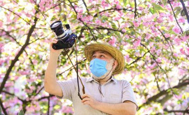 Turist kamerası fotoğrafı. Doğa fotoğrafçılığı. Suni solunum maskesi. Profesyonel fotoğrafçı koronavirüs karantinasında çalışıyor. Salgın hastalık konsepti. Tehlikeli fotoğrafçı. Çalışmaya devam. Polen alerjisi