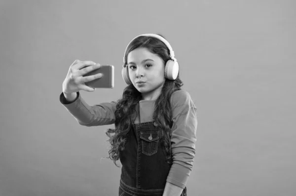 Νιώθω παιχνιδιάρης και αστείος. μικρό παιδί βιντεοκλήση στο smartphone. μικρό κορίτσι κρατήσει το κινητό τηλέφωνο. blogging στη σύγχρονη ζωή. Μαθήτρια χρησιμοποιεί νέα τεχνολογία. ζουν σε εικονικό κόσμο. παιδί selfie στα ακουστικά — Φωτογραφία Αρχείου