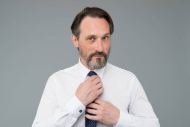 Hırslı ve yakışıklı. Sakallı olgun bir adam. Sabah bakım rutini. Olgun iş adamı kravatı düzeltir. Orta yaşlı beyaz erkek yönetici iş başında. Patron toplantı için hazırlan. Erkek ofis modası