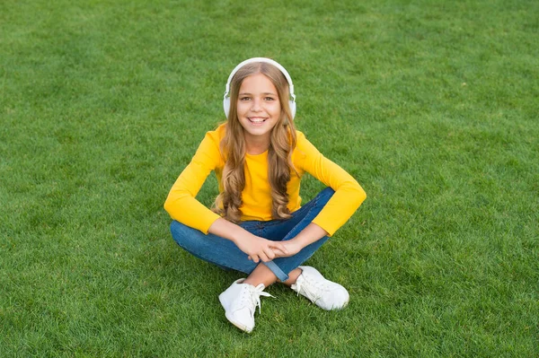 緑の芝生でリラックス。春のレジャータイム。幸せな子供時代。ヘッドセットの子供だ。幸せな女の子は好きな歌を聞く。子供の美しさとファッション。10代の女の子は屋外で音楽を聞く。自然界の音 — ストック写真