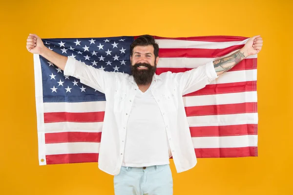 Firar självständigheten. Glad hipster firar självständighetsdagen. Skäggig man hålla amerikansk flagga gul bakgrund. Självständighetsdagen. Fjärde juli. Nationernas oberoende — Stockfoto