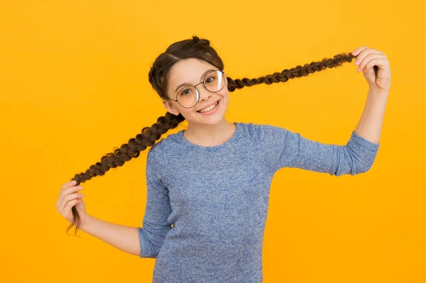 Interessado no meu cabelo e no meu cabeleireiro. Menina feliz segurar tranças de cabelo fundo amarelo. Criança pequena com cabelo comprido. Barbeiro de crianças. Salão de cabeleireiro. Produtos de cuidados com os cabelos e cosméticos — Fotografia de Stock