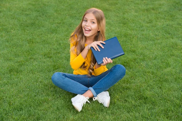 Escribir recuerdos de la infancia. Niño leer libro en el parque. estudio de niña feliz en vacaciones. Moda de belleza infantil. adolescente chica inspirada con nuevo libro. relajarse en la hierba verde. tiempo libre de primavera. feliz infancia — Foto de Stock