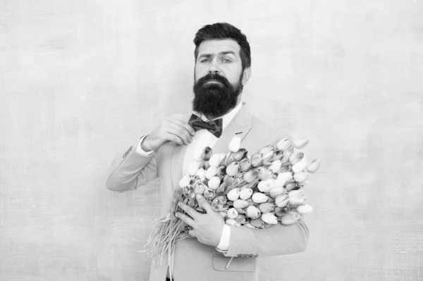Feliz día de las mujeres. El hombre barbudo sostiene flores de primavera. Ramo de tulipanes para el día de las mujeres. Hipster usa traje formal y pajarita. Listo para la celebración del día de las mujeres. 8 de marzo. Vacaciones internacionales para mujeres —  Fotos de Stock