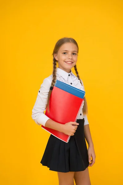 Nivel básico. La colegiala feliz tiene libros de texto de fondo amarillo. La colegiala vuelve a la escuela. Una colegiala pequeña usa uniforme. Linda colegiala. Educación escolar. Cursos para niños dotados —  Fotos de Stock