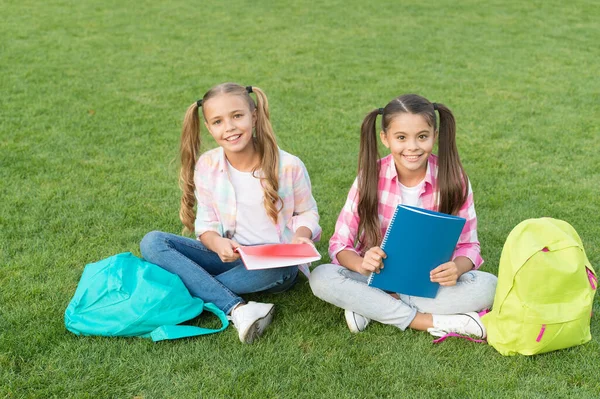 知识的日子来了。在绿草上玩得开心。两个背着背包的小孩。小女孩在课间休息时玩耍和学习。孩子们快乐的一天。姐妹关系和家庭观念。夏天快乐 — 图库照片