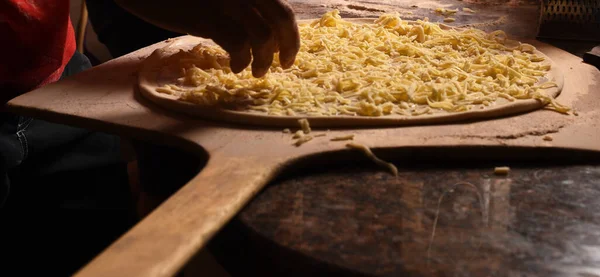 Pizza com queijo em tábua de madeira. Pizzaiolo põe queijo — Fotografia de Stock