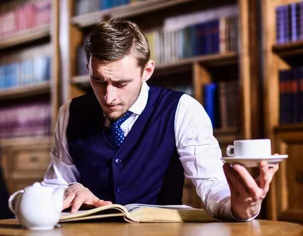 Five oclock tea tradition concept. Young man with antique bookshelves