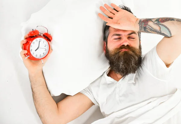 El hombre con la cara somnolienta yace en la almohada, sostiene el despertador . —  Fotos de Stock