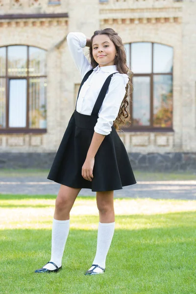 En bra klädsel. Glad skolflicka i snygg uniform. barndoms lycka. vintage barnmode. liten student flicka koppla av på grönt gräs. Tillbaka till skolan. liten flicka ser smart och intelligent — Stockfoto