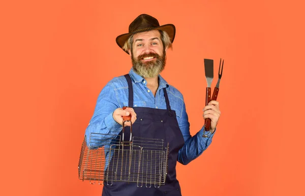 Spring season. Bearded hipster wear hat and apron for barbecue. Roasting meat. Picnic and barbecue. Steak and barbecue. Barbecue menu. Grilling food. American picnic. Family tradition. Cooking meat