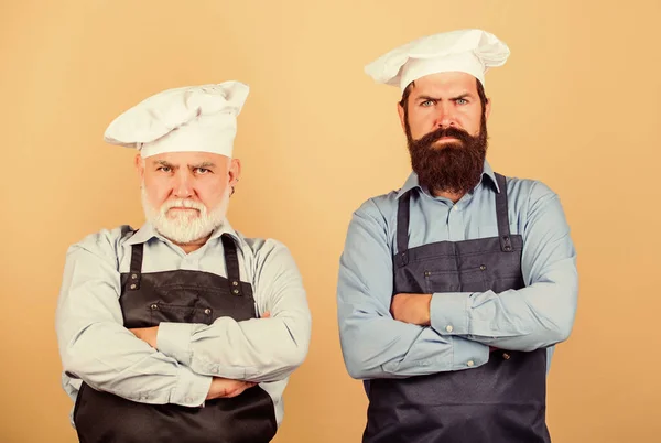 Aile yemeği. Baba ve oğul birlikte yemek pişiriyorlar. Restoranda ticari mutfak. Profesyonel şefler. Aşçı şapkalı adamlar. Olgun sakallı şef. Yemek yapmaktan yoruldum. Mutfağın efendileri. En iyisi kim? — Stok fotoğraf