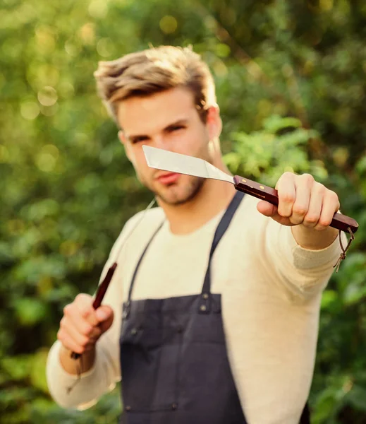 Cucinare hamburger. Concetto picnic. Bbq chef. Un bel ragazzo che cucina cibo. L'uomo tiene attrezzature per barbecue. Cibo grigliato. Utensili da barbecue. Weekend estivo. Strumenti per arrostire carne all'aperto. Festa barbecue — Foto Stock