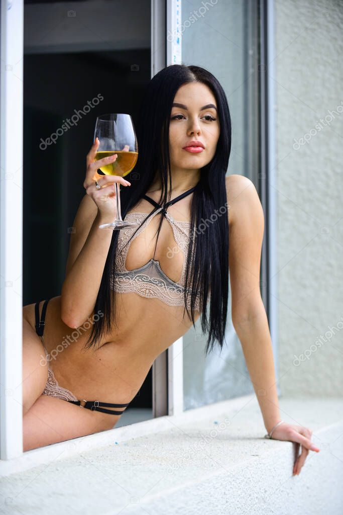 Hedonism concept. Woman drink wine. Sexy girl with alcohol cocktail. Sexy girl with glass of wine. Hot lady in erotic lingerie sit window sill. Home party. Elite wine. She knows a lot about pleasure