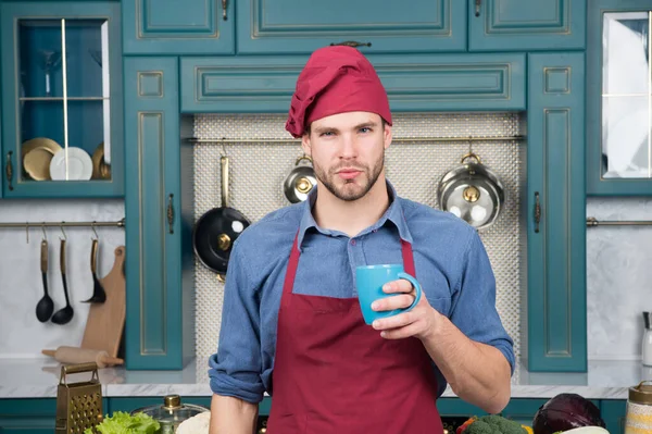 Maar eerst koffie. Een man met een koffiekop. Koken proces concept. Kok in bordeaux uniform drinkt koffie voor inspiratie. Kok staat naast tafel met ingrediënten en keukengerei. Zelfverzorging — Stockfoto