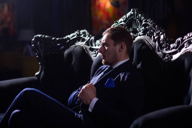 Boss in fashionable suit looks confident. Businessman sits on elegant vintage sofa and thinks.