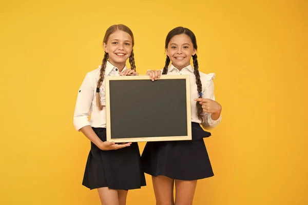 Schrijftijd. Kleine meisjes houden zwarte schrijfoppervlak op gele achtergrond. Kleine kinderen wijzend vinger op schoolbord voor het schrijven van informatie. Blanco bord voorschrijven, ruimte kopiëren — Stockfoto